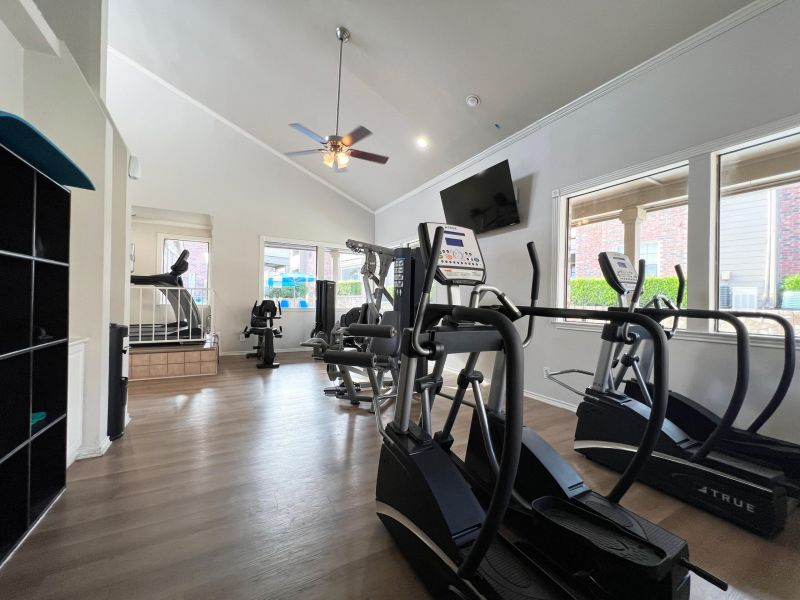 Ashwood Park modern gym room with cardio machines, large windows, TV, and wooden floors.