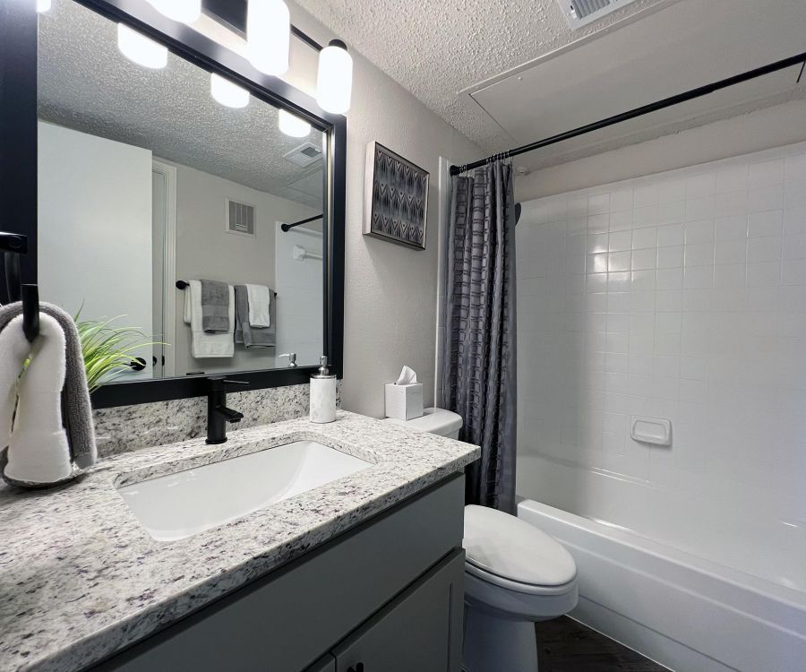 Ashwood Park modern bathroom with a granite countertop, gray cabinets, and a shower with white tiles and a gray curtain.