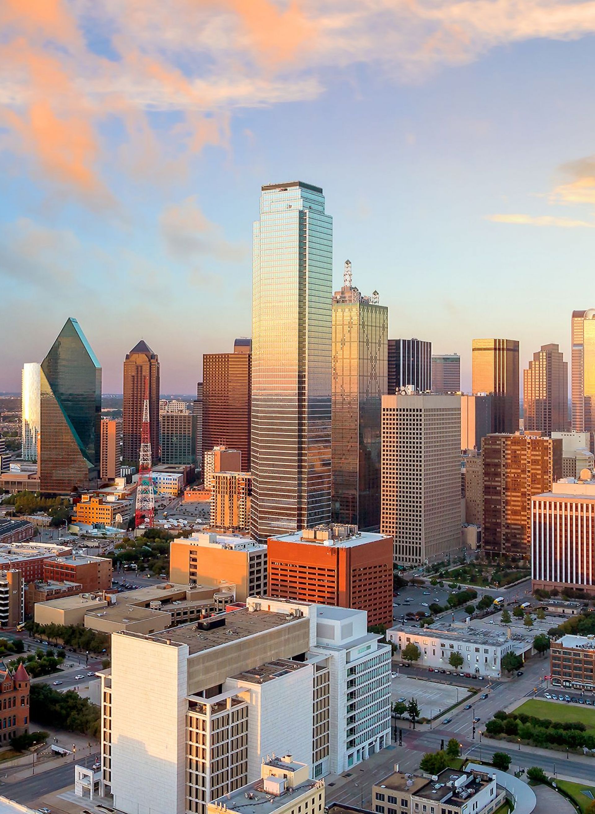 Aerial view of a city skyline at sunset, with tall buildings and a colorful sky.