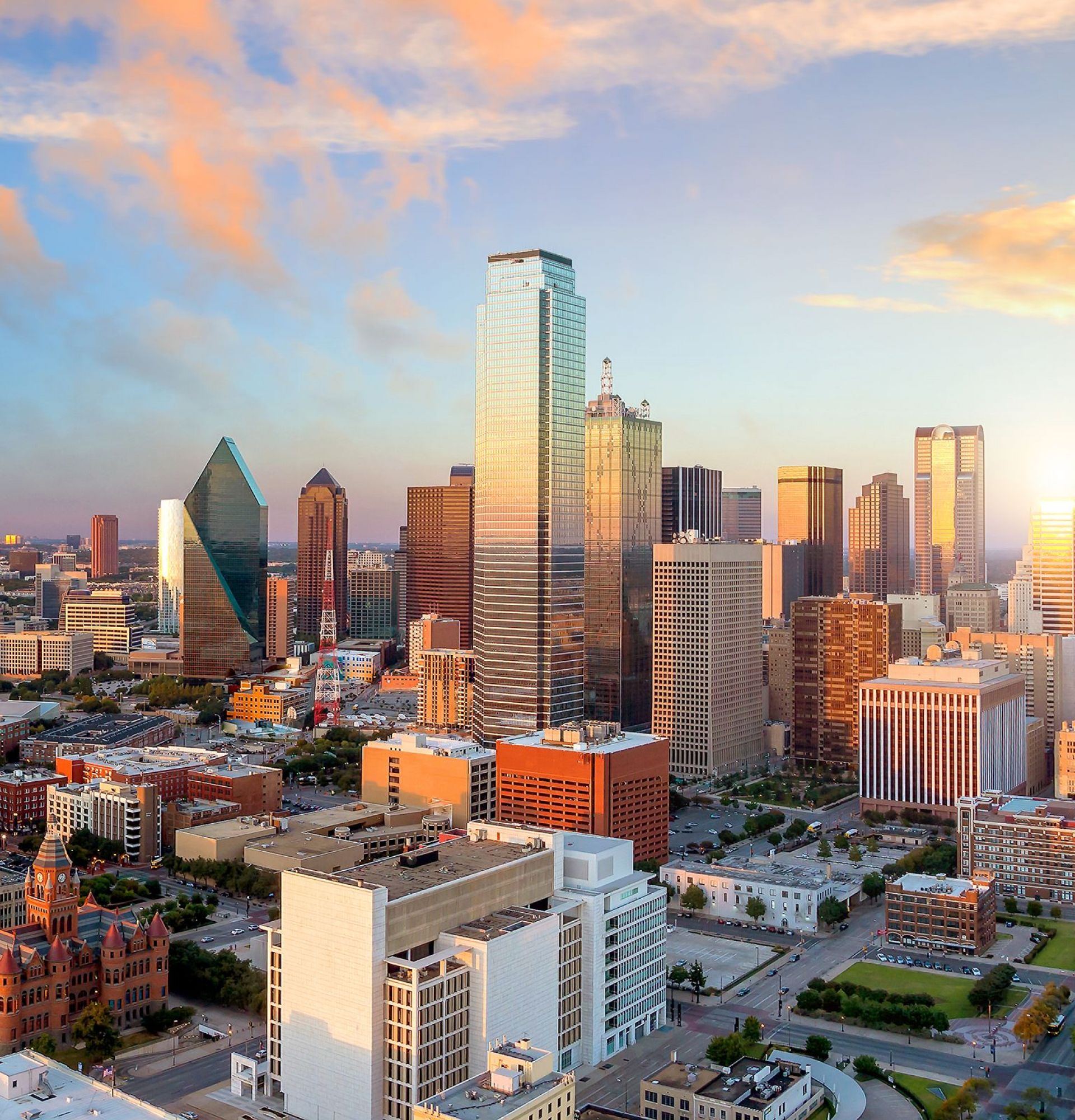 Aerial view of a city skyline at sunset, with tall buildings and a colorful sky.