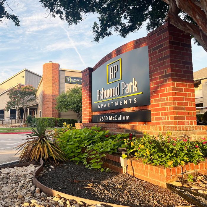 Entrance sign for Ashwood Park Apartments, surrounded by plants and landscaping, with buildings in the background.
