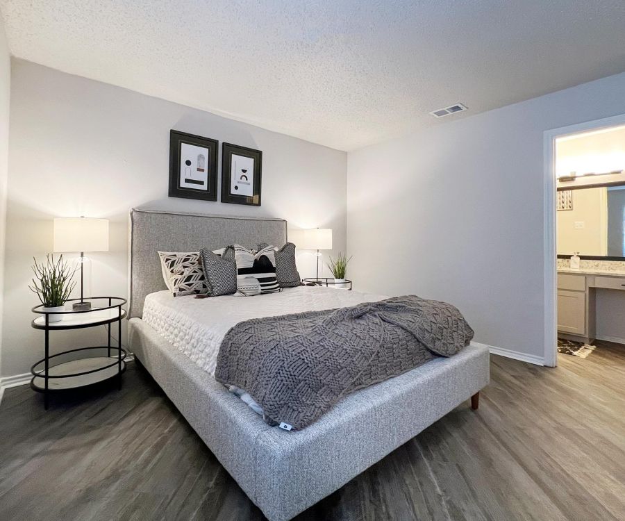 Ashwood Park modern bedroom with a gray bed, two bedside tables with lamps, and an open door to a well-lit bathroom.