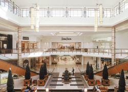 Interior of a spacious shopping mall with Neiman Marcus, two levels, escalators, and decorative plants.